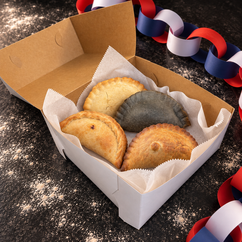 Open Family Box with four gluten free ingredients empanadas on a flour-dusted black counter with Chilean red, white and blue decoration